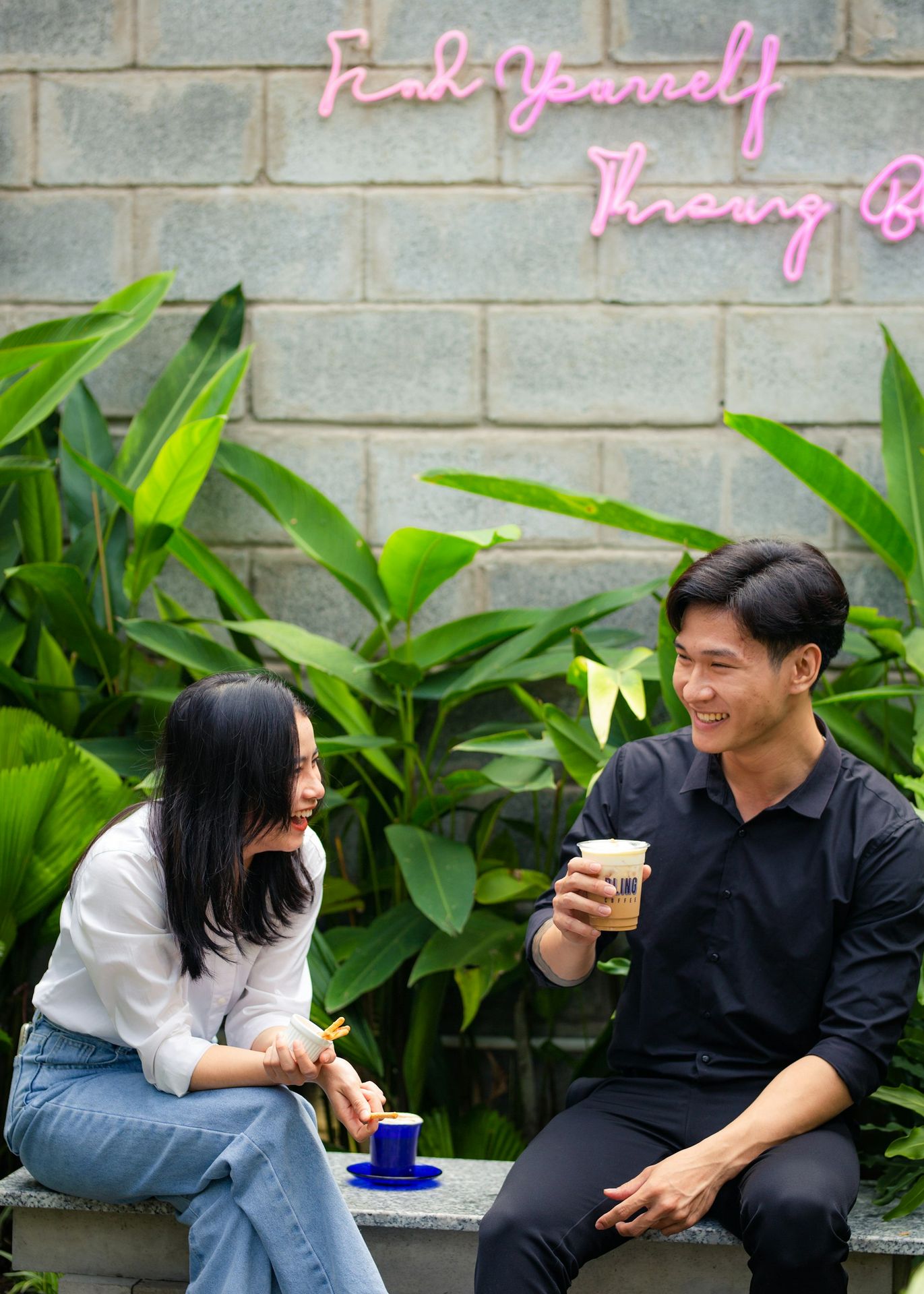 a man and a woman sitting on a bench drinking coffee